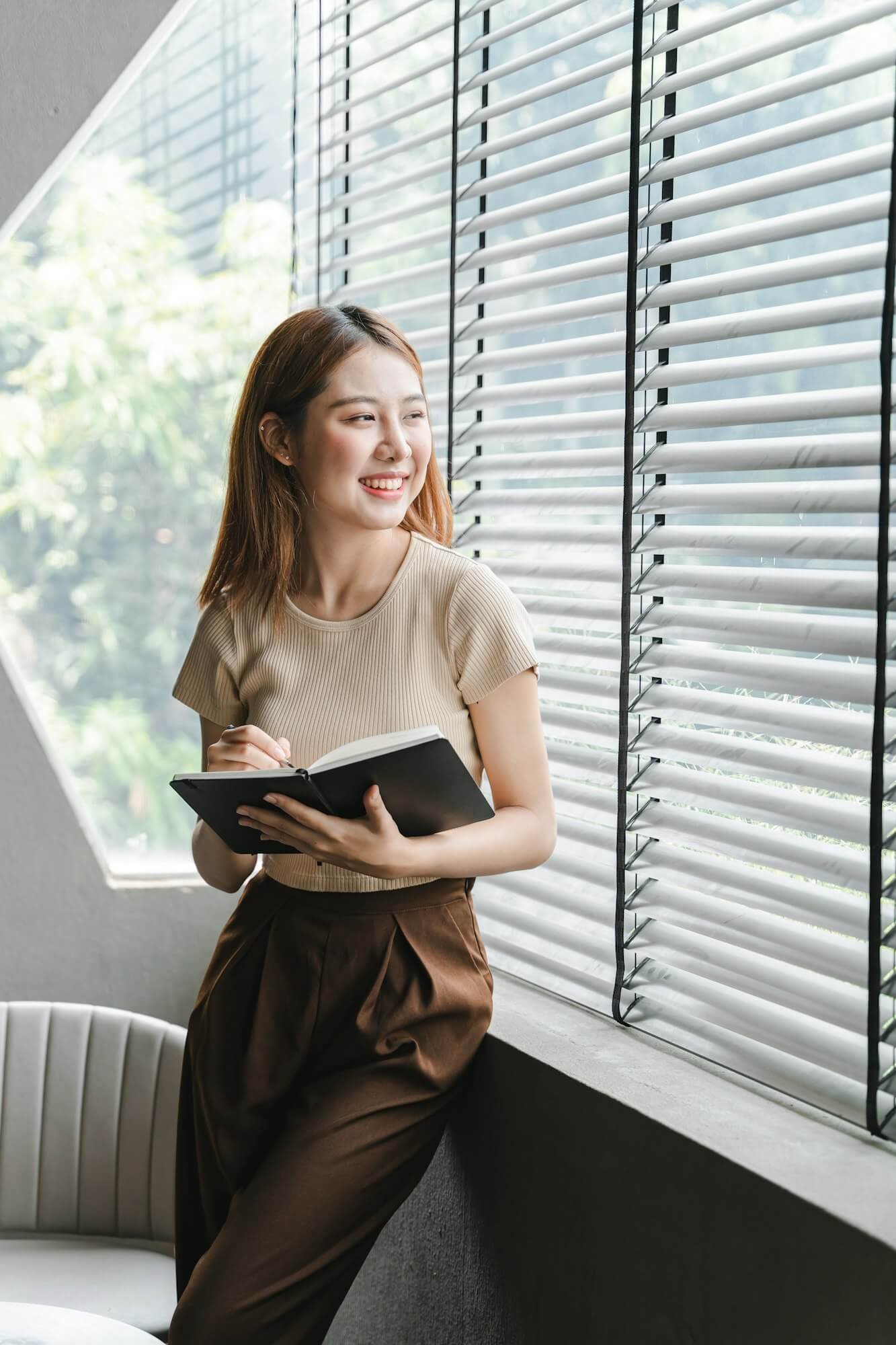 smiling-asian-woman-holding-a-note-in-hand-and-standing-near-window-startup-business-asian-woman-onl.jpg